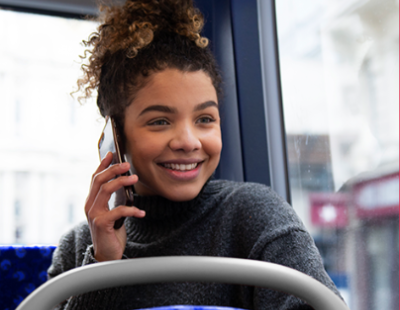 Image of smiling teenager sitting on a bus and talking on her mobile phone.