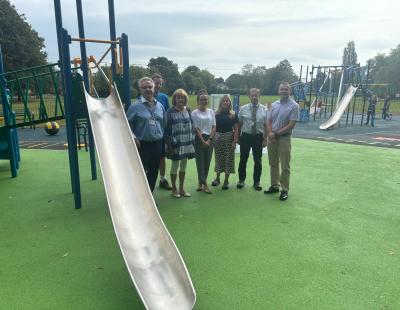 Image of a group of 6 male and female council members, officers and parish councillors standing next to a new slide at Culcheth Village Green play area. 