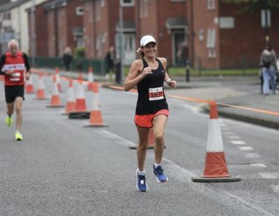 Image of Jenny Hibbert, in athletics kit, running through the streets during the Warrington Running Festival.