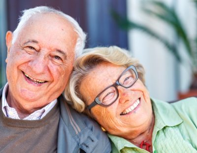 Photo of man and woman facing the camera, man is smiling towards the camera, female is leaning on male's shoulder