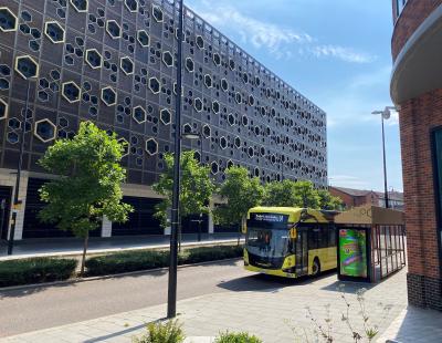 Image of one of Warrington's yellow electric buses driving past the Time Square multi-storey car park.